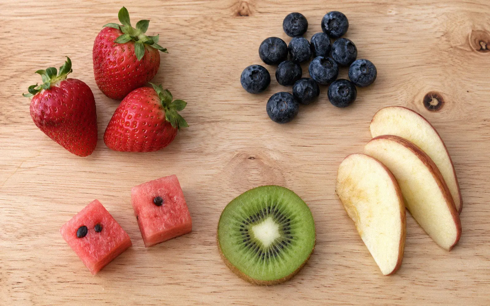 Safe fruit alternatives for guinea pigs including strawberries blueberries apple slices and watermelon cubes arranged as healthy lemon alternatives